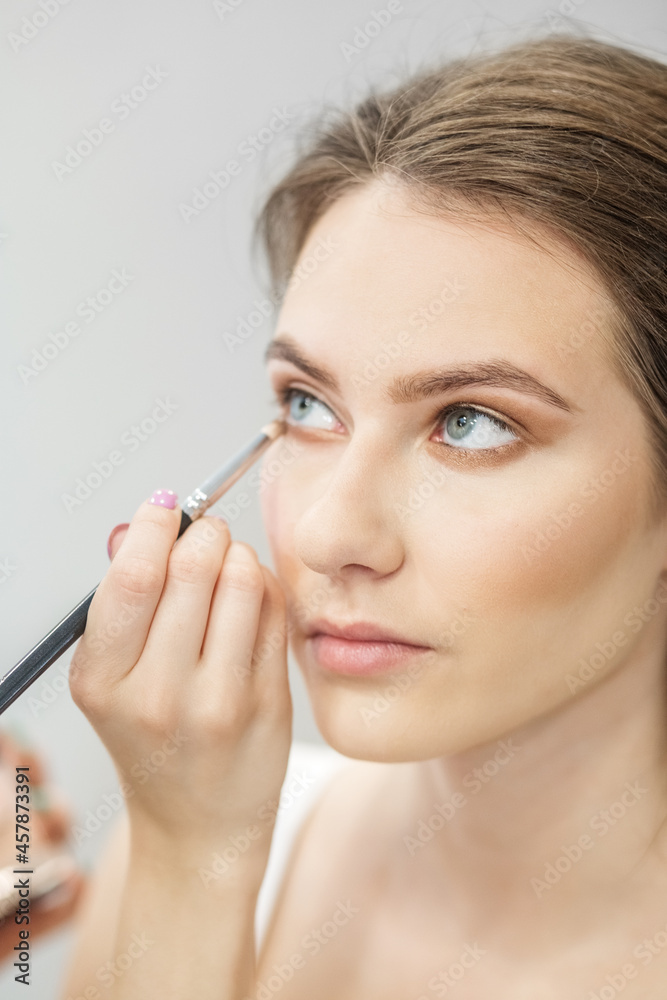 Makeup artist makes makeup to a girl. Apply beige eye shadow. Close-up. Vertical