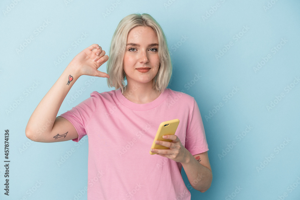 Young caucasian woman holding mobile phone isolated on blue background showing a dislike gesture, thumbs down. Disagreement concept. Young caucasian woman holding mobile phone isolated on blue background showing a dislike gesture, thumbs down. Disagreement concept.