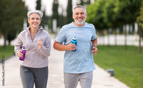 Lovely joyful retirees couple jogging outside in city park