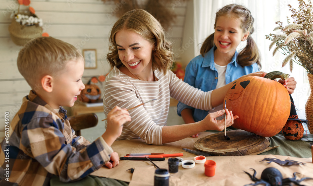 Fototapeta premium Smiling mother with children creating jack-o-lantern during Halloween celebration at home