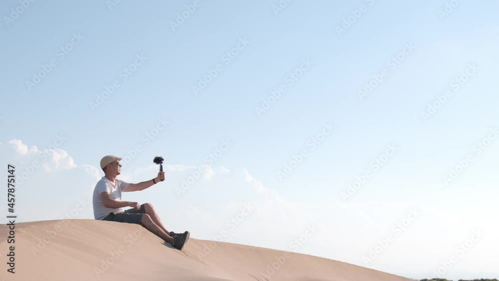 Man filming himself with his cell phone in the desert dunes. Traveling male content creator