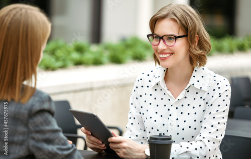 Smiling woman with digital tablet in hand discussing startup with business partner in outdoor cafe