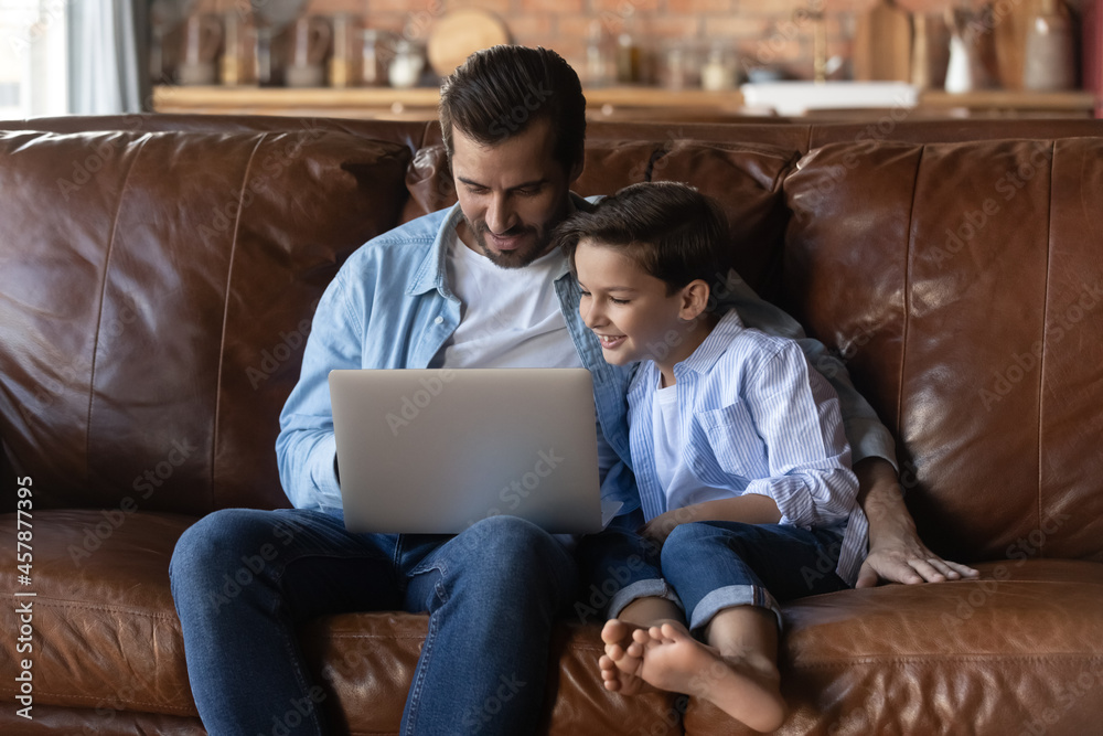 Caring father with little son hugging, using laptop together, relaxing sitting on couch at home, loving dad and 8s boy kid watching cartoons or funny video, chatting online, enjoying leisure time Caring father with little son hugging, using laptop together, relaxing sitting on couch at home, loving dad and 8s boy kid watching cartoons or funny video, chatting online, enjoying leisure time