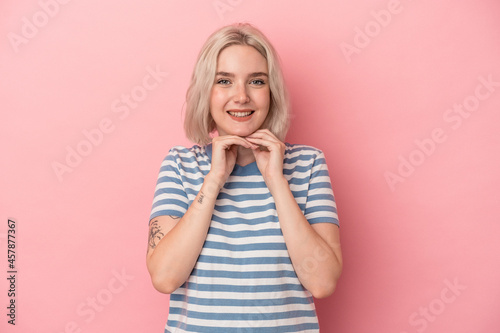 Young caucasian woman isolated on pink background keeps hands under chin, is looking happily aside.