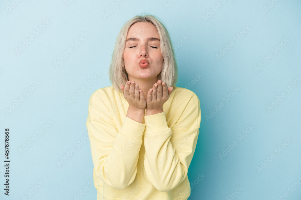 Young caucasian woman isolated on blue background folding lips and holding palms to send air kiss.
