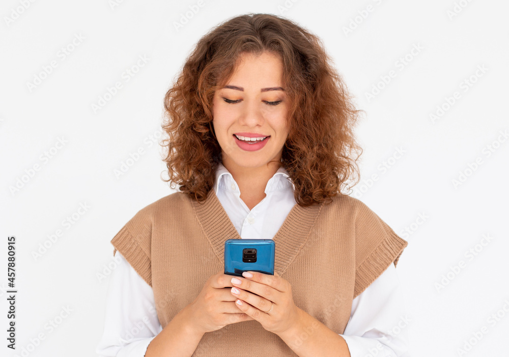 Curly smiling young woman demonstrating white teeth using cell phone, messaging, being happy to text with her boyfriend, looking at screen of smartphone. Modern technologies and communication Curly smiling young woman demonstrating white teeth using cell phone, messaging, being happy to text with her boyfriend, looking at screen of smartphone. Modern technologies and communication