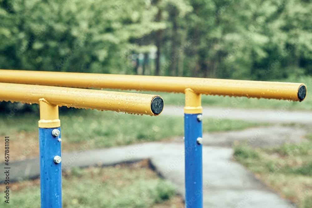 Yellow metal bars for exercises with hanging rain drops at sports ground in spring green park on cloudy day extreme close view Yellow metal bars for exercises with hanging rain drops at sports ground in spring green park on cloudy day extreme close view