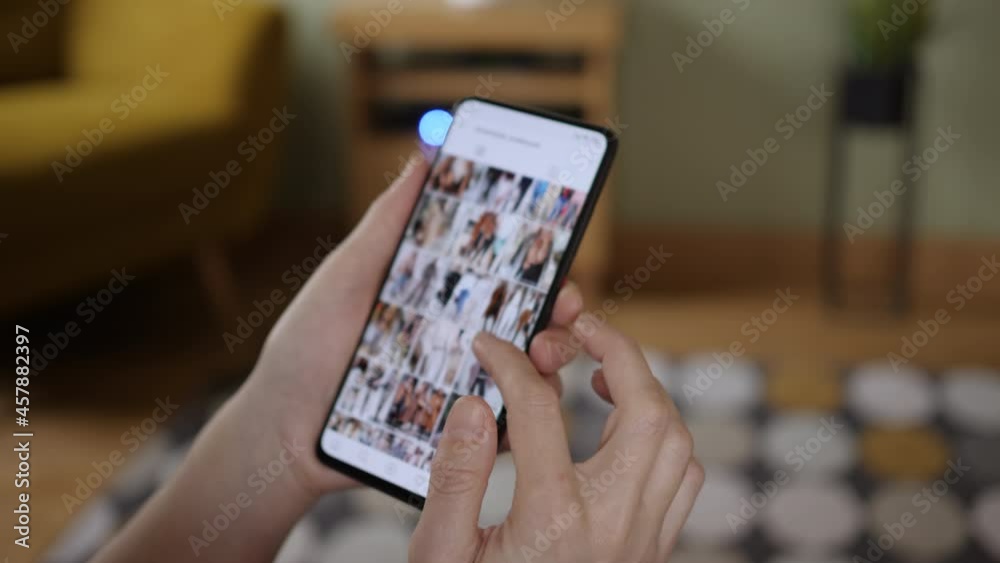 Girl Looks Social Network Page On Mobile Phone. Woman Browsing Fashion Trends on Smartphone. Woman at Home Lying on Couch Using Smartphone Scrolling Through Social Network Feed.
