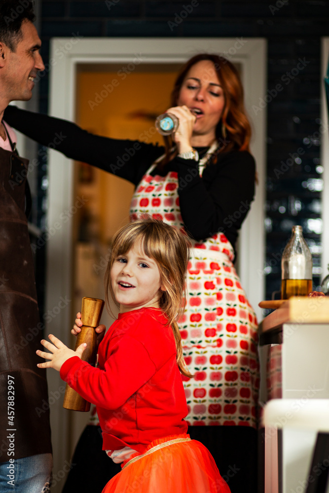 Fototapeta premium Beautiful happy family in the kitchen. Beautiful red hair young woman, handsome man and cute little girl, having fun at home, in the kitchen.