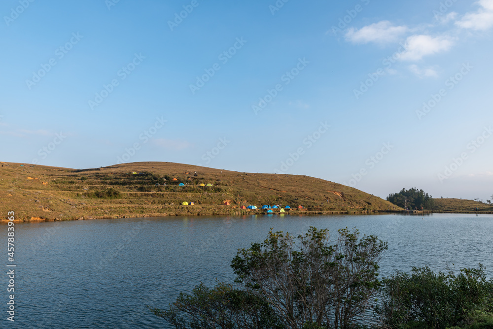 In the lake on the grassland, people set up tents by the lake