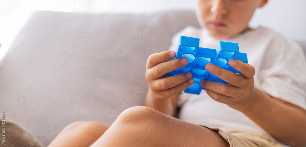 Child plays with blue pop-it in form of puzzle. Cheerful boy holds in his hands a blue toy anti-stress pop it. Little blonde boy playing with new trend sensory toy - pop it. Child plays with blue pop-it in form of puzzle. Cheerful boy holds in his hands a blue toy anti-stress pop it. Little blonde boy playing with new trend sensory toy - pop it.
