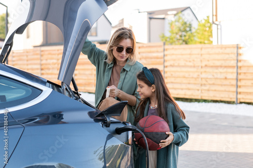 Photography Little girl and young woman standing by trunk while charging electric car at sta