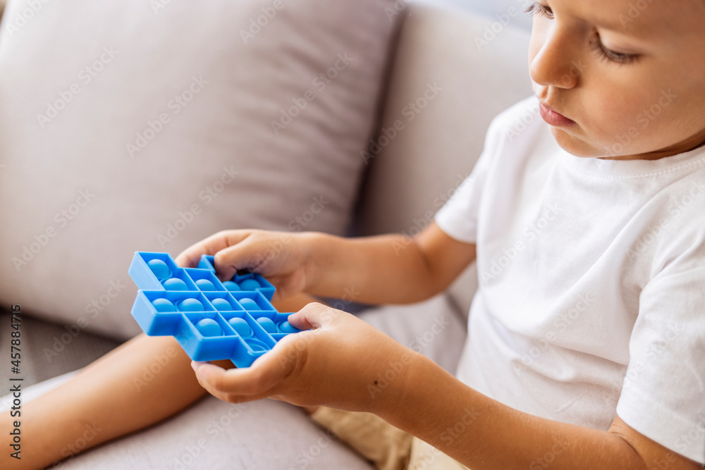 Boy lying on the couch and playing with sensory pop it fidget toy at home. Kid playes stress and anxiety relief fidgeting game. Boy with pop it a heart shape sensory toy. Boy lying on the couch and playing with sensory pop it fidget toy at home. Kid playes stress and anxiety relief fidgeting game. Boy with pop it a heart shape sensory toy.
