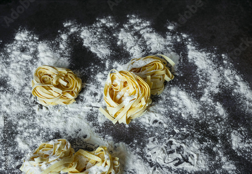Raw Tagliatelle's handmade pasta with flour on a dark table