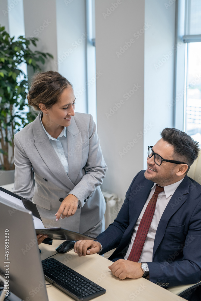 Elegant young secretary showing business documents to her boss in office Elegant young secretary showing business documents to her boss in office