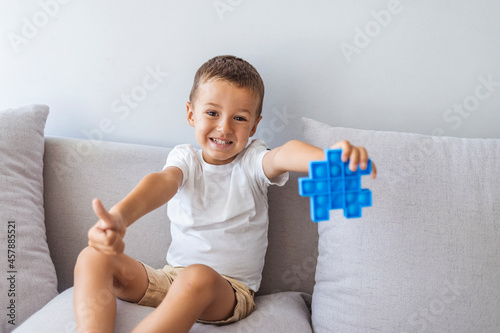 Boy smiling and playing with blue pop it fidget toy. Push bubble fidget sensory toy - washable and reusable stress relief toy. Antistress toy for child with special needs. Mental health concept photo