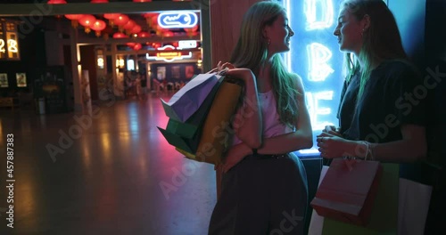 Two young beautiful lady walking after successful shopping, they smile and carry colour packages in their hands. Stylish girls walking around the mall and have fun. An exciting conversation between photo