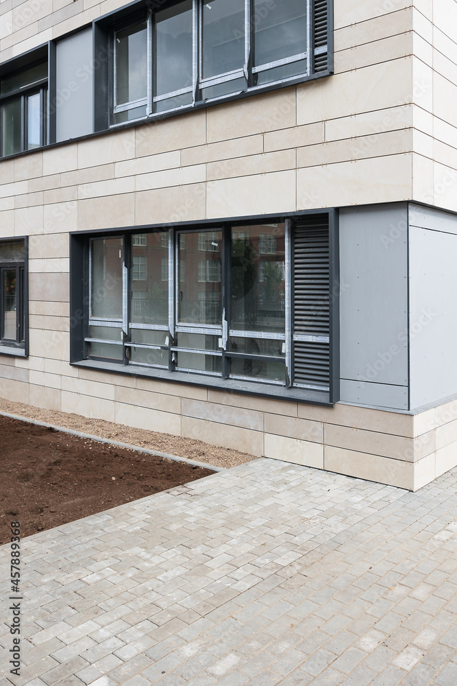 Construction and improvement of the local area. Lawn preparation and sowing with grass. Ground floor of an apartment building and beige ventilated facade. Porcelain stoneware on the wall of the house.