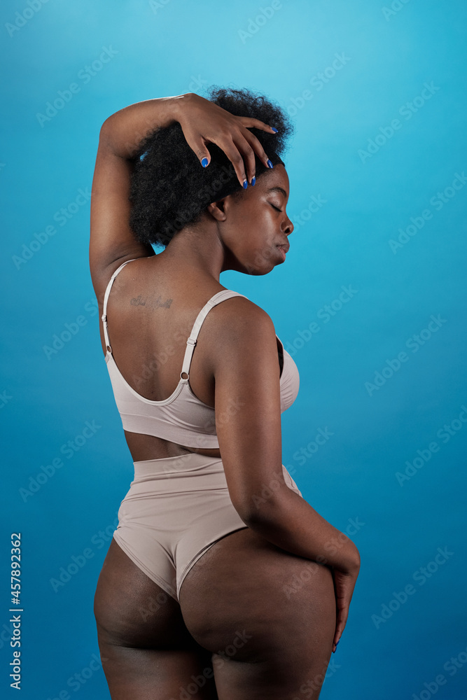 Obraz premium Rear view of plus size woman in underwear touching her hair and keeping eyes closed
