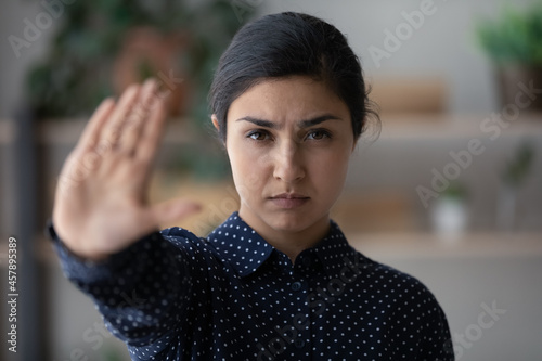 Head shot portrait serious Indian woman showing stop gesture and looking at camera, strong young female protesting against domestic violence and abuse, bullying, saying no to gender discrimination photo