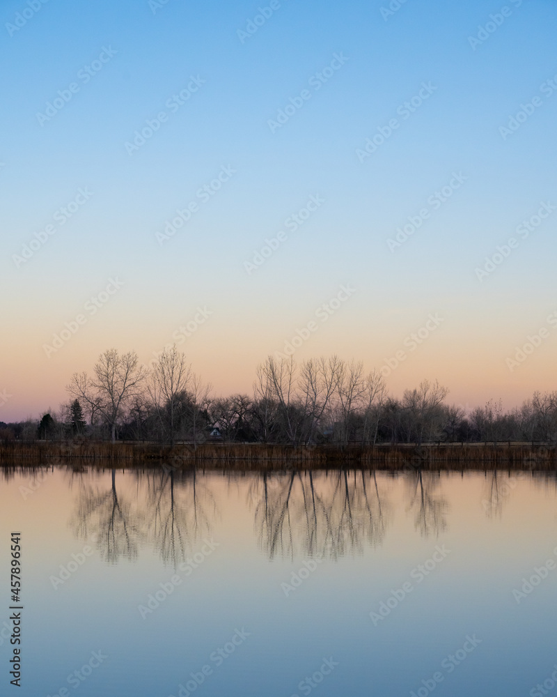 Obraz premium Trees reflect off a smooth pond at sunset