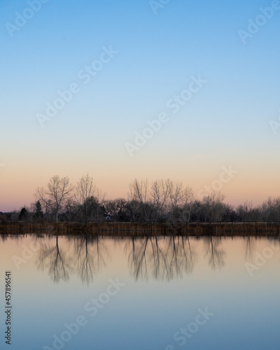 Trees reflect off a smooth pond at sunset