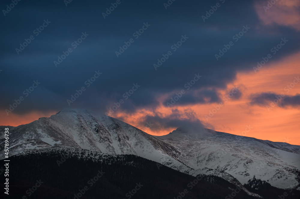 Orange sunset behind foreground clouds and the Continental Divide near Winter Park, Colorado