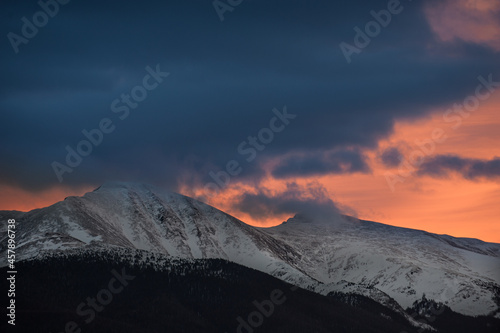 Orange sunset behind foreground clouds and the Continental Divide near Winter Park, Colorado