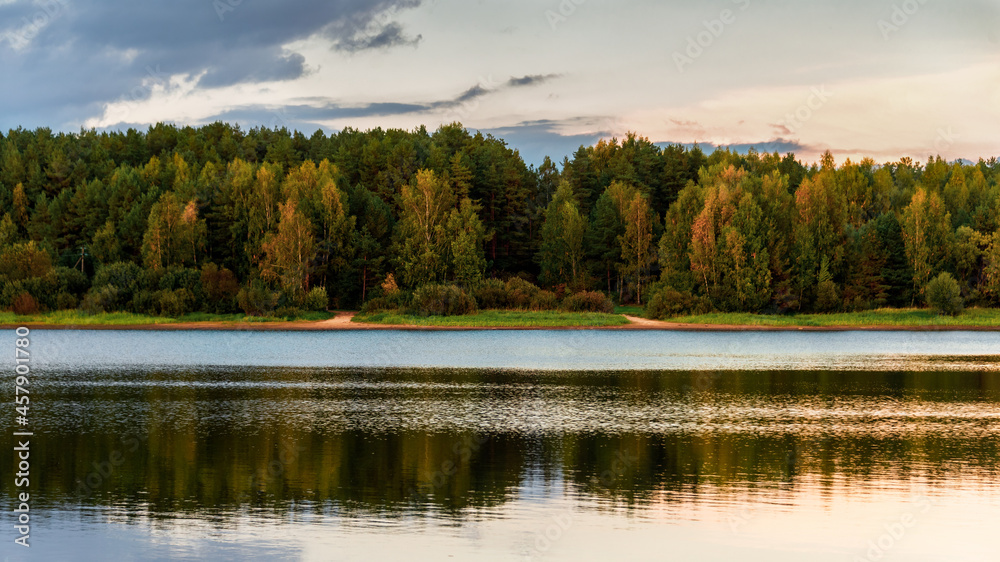 Landscape with a river and a forest illuminated by the setting sun. Reflection of clouds in the water. Landscape with a river and a forest illuminated by the setting sun. Reflection of clouds in the water.