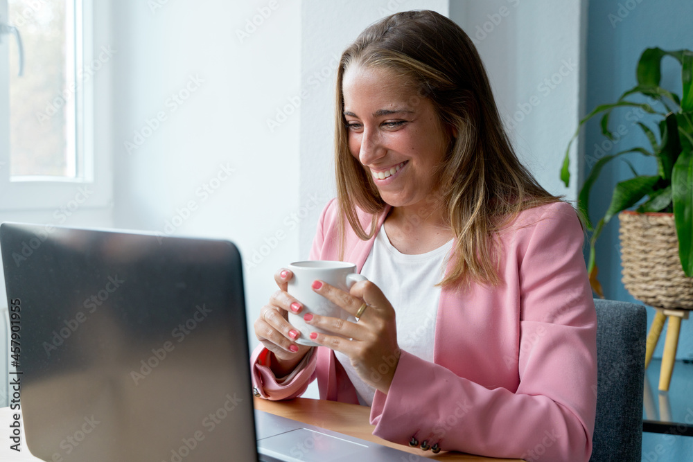 Middle view of caucasian woman working with laptop at home. Horizontal side view of blonde woman drinking coffee and working with computer indoors. Online working and technology concept. Middle view of caucasian woman working with laptop at home. Horizontal side view of blonde woman drinking coffee and working with computer indoors. Online working and technology concept.