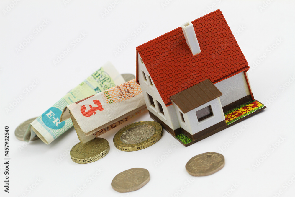 Model house with British pound notes and coins on white background