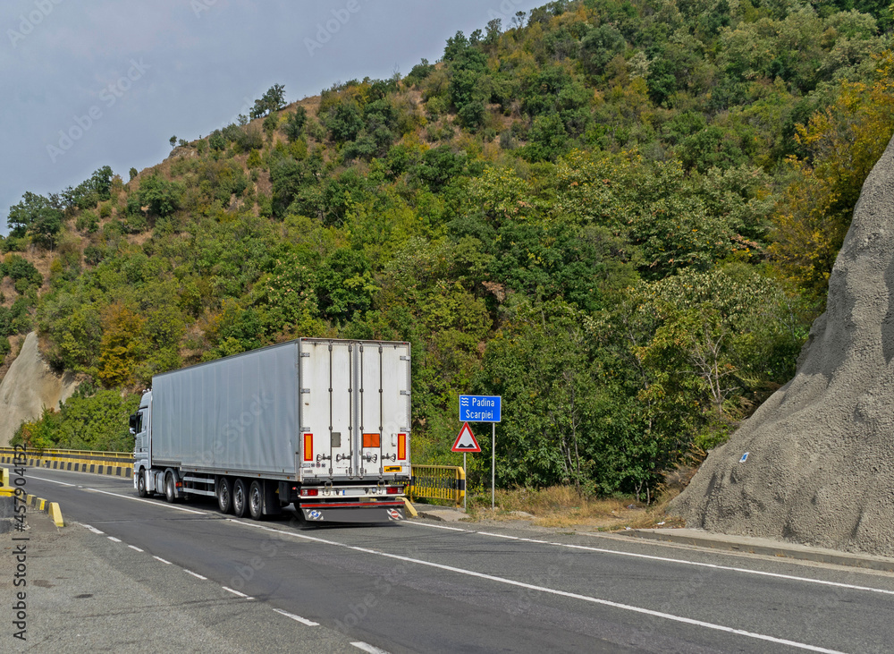 Truck transporting goods moving on a beautiful road near the mountain. Truck carrying various goods. No logo or brand. Truck transporting goods moving on a beautiful road near the mountain. Truck carrying various goods. No logo or brand.