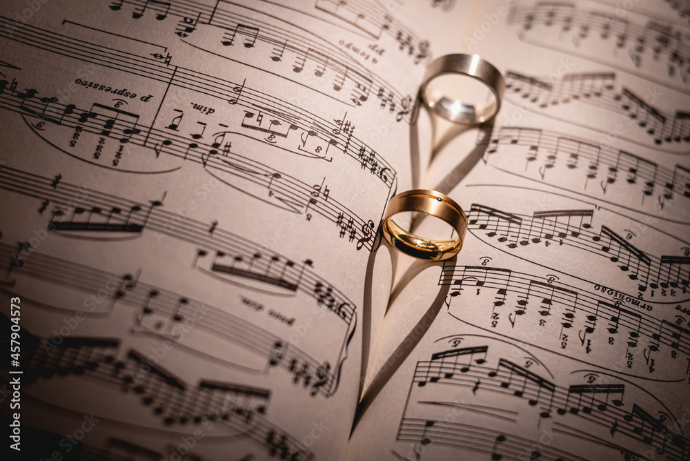 Two matt wedding rings one silver one golden on a book with sheet music. Two rings on sheet notes forming a heart. Ring and heart Two matt wedding rings one silver one golden on a book with sheet music. Two rings on sheet notes forming a heart. Ring and heart