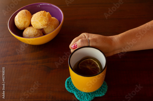 Uma mão feminina segurando uma caneca de chá e uma vasilha de pães de queijo. photo