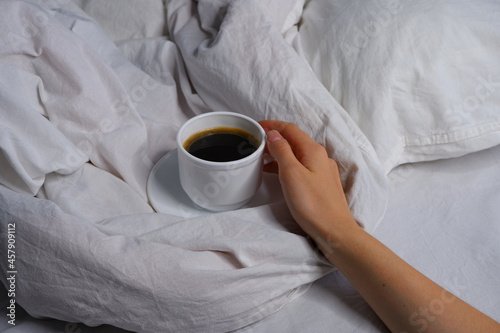 Girl holding a cup of coffee in bed. Breakfast in bed. Interior. Cosiness.
