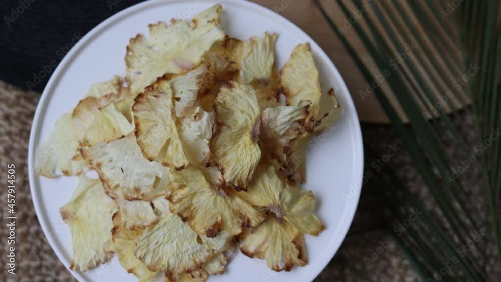 Organic dried fruits. Homemade dehydrated pineapple fruit chips on a white round tray. A round black napkin and a palm leaf. The concept of healthy eating. dried pineapple top view. Organic dried fruits. Homemade dehydrated pineapple fruit chips on a white round tray. A round black napkin and a palm leaf. The concept of healthy eating. dried pineapple top view.