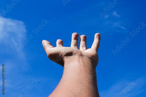 An Asian Man Hand Gesture Trying to Reach the Sky with Clear Blue Sky on a Sunny Day to Illustrate Dream Catcher, Success, and Struggle