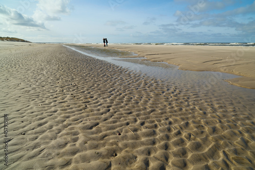 Jesienny, zimowy spacer nas morzem. W oddali spacerujące dziewczyny. Ujęcie obiektywem szerokokątnym. Pomarszczona powierzchnia plaży. Po sztormie.
