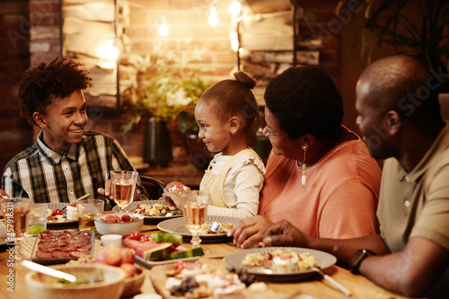 Warm toned portrait of happy African-American family enjoying dinner together outdoors with focus on smiling kids