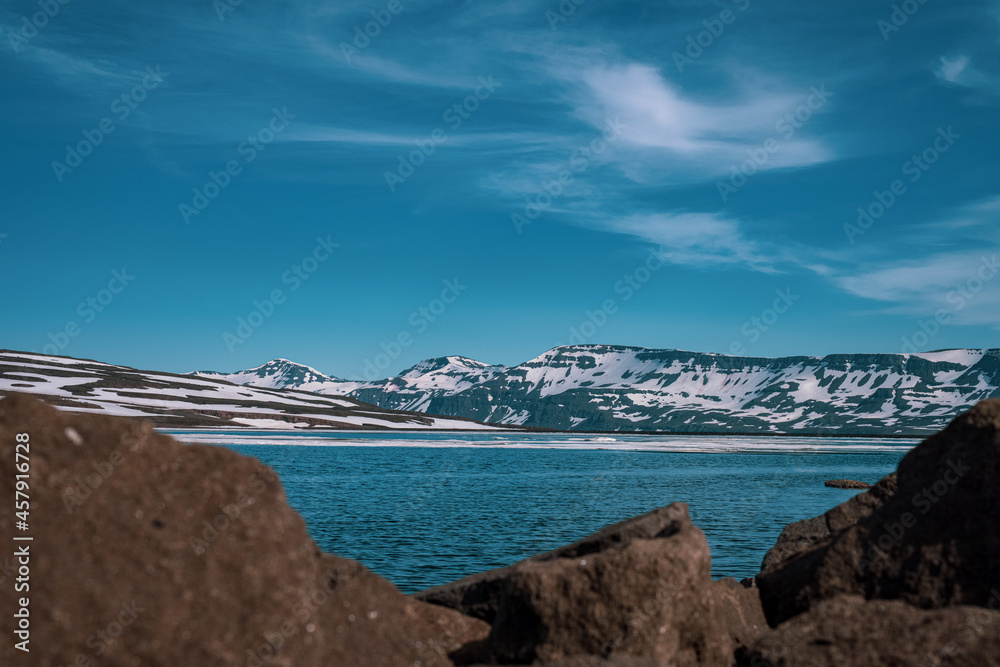 Fototapeta premium Panoramic frog view of Heidharvatn lake in eastern iceland, glacial lake with some blocks of ice floating and majestic mountains and road next to it.