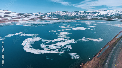 Aerial drone view of Heidharvatn lake in eastern iceland, glacial lake with some blocks of ice floating and majestic mountains and road next to it. © Anze