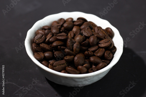 Coffee beans in a white plate on a black background.