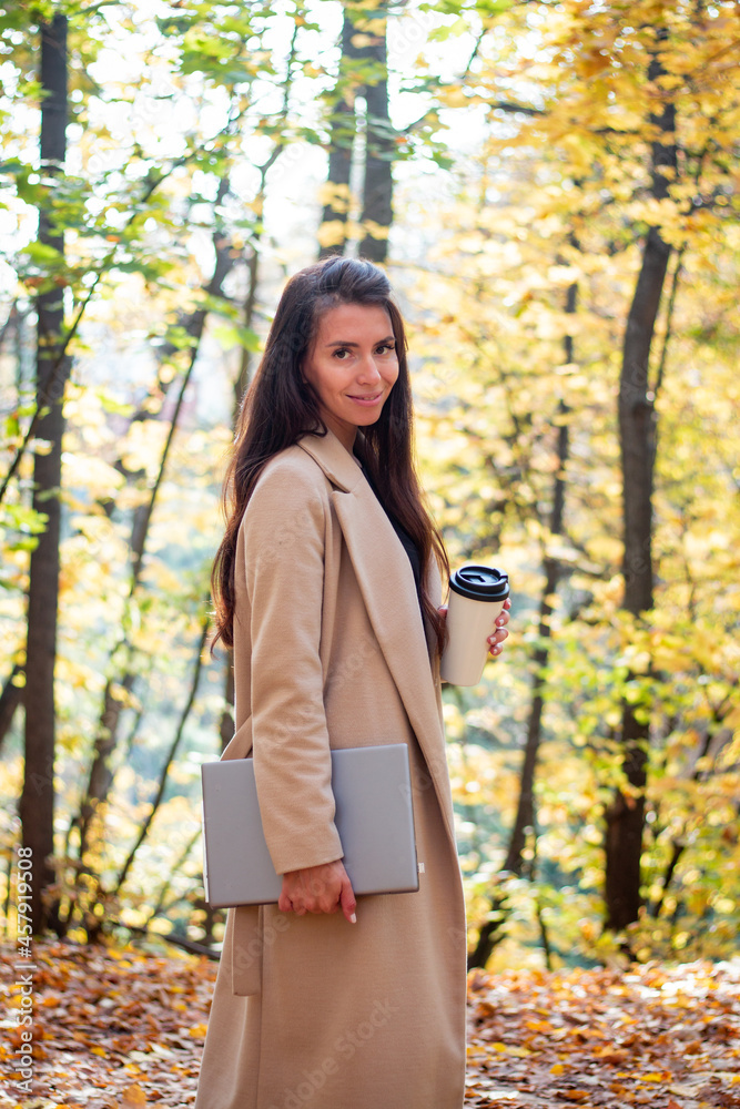 Brunette woman in autumn park with laptop and cup of coffee. Student. Teacher. Online education. Brunette woman in autumn park with laptop and cup of coffee. Student. Teacher. Online education.