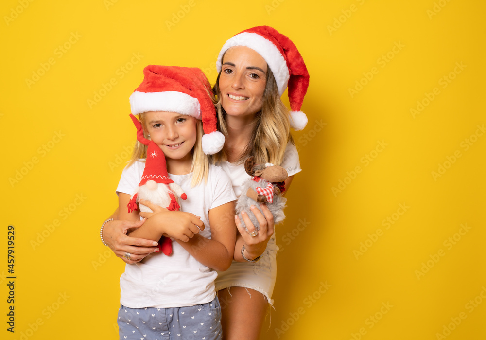 Happy mother and daughter in santa hat over yellow background. Christmas season concept. Happy mother and daughter in santa hat over yellow background. Christmas season concept.