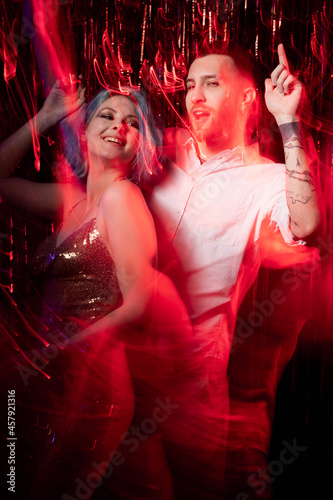 Wedding party. Happy beloved couple. Celebration fun. Enjoying moment. Cheerful man and woman dancing together long exposure red neon light motion waves blur cascade curtain background.