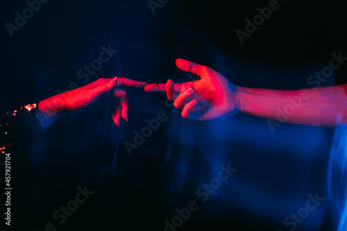 Love power. Romantic couple. Affectionate feelings. Happy meeting. Sensual male and female hands reaching together on blue red neon light blur long exposure isolated black.
