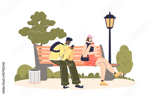 Young couple sit on bench in park using smartphones chatting and messaging online outdoors