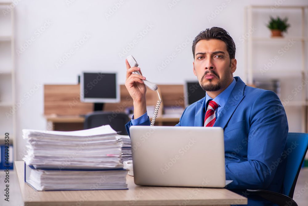 Young male employee unhappy with excessive work at workplace Young male employee unhappy with excessive work at workplace