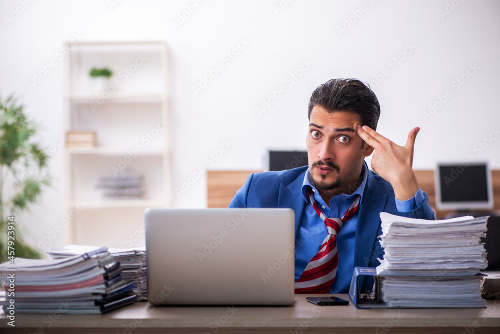 Young male employee unhappy with excessive work at workplace Young male employee unhappy with excessive work at workplace