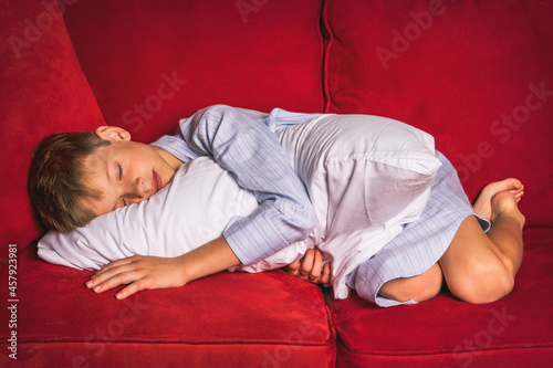 Young boy in nightshirt sleeping on plush red sofa photo